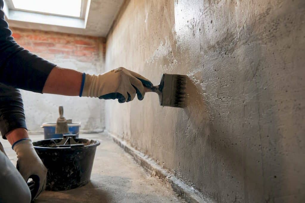 Brush applying crystalline waterproofing to basement wall